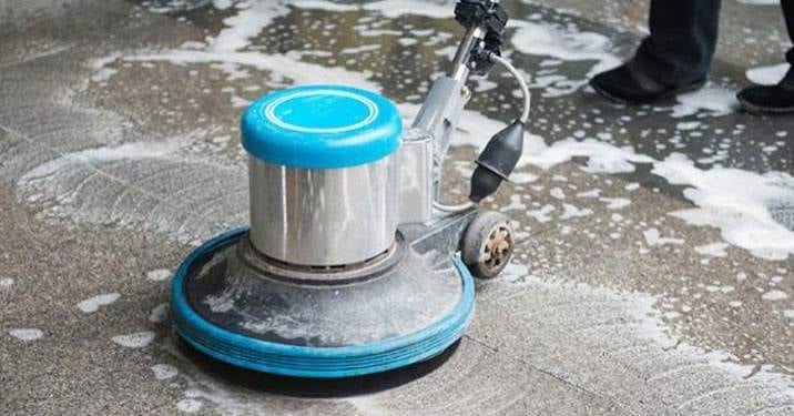 Blue and silver floor cleaning machine with rotating pad on wet concrete ground